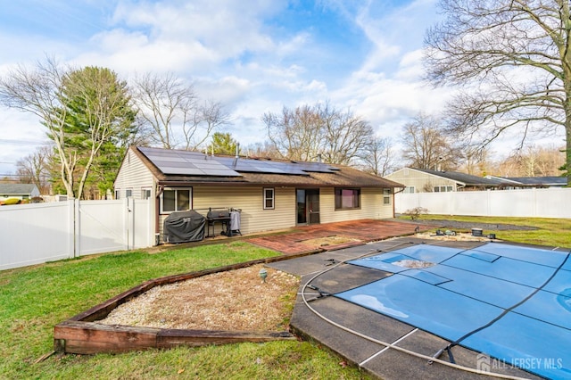 rear view of house featuring solar panels, a lawn, a fenced backyard, and a gate