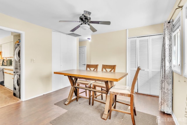 dining space featuring light wood-type flooring, stacked washer and dryer, ceiling fan, and visible vents