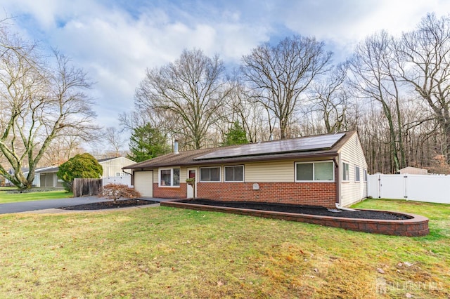 ranch-style home featuring brick siding, a gate, roof mounted solar panels, fence, and driveway