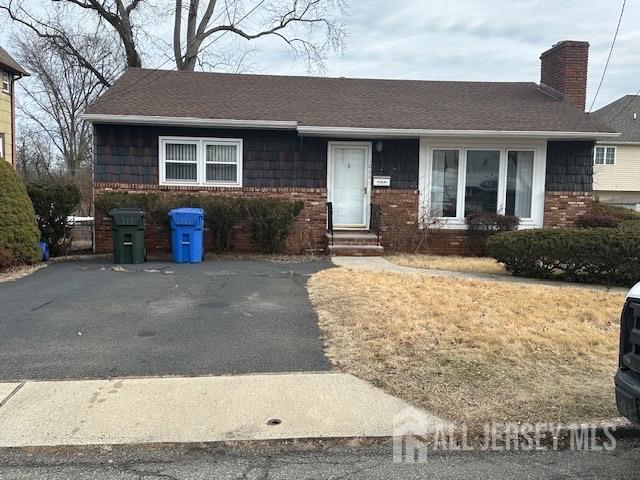 single story home featuring brick siding, entry steps, a chimney, and a shingled roof