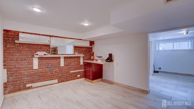 kitchen featuring baseboards, brick wall, and light countertops