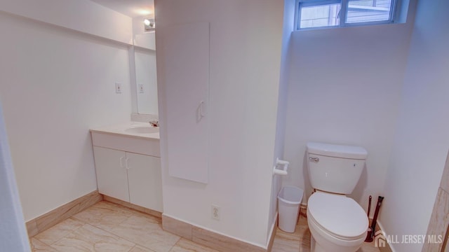 bathroom with marble finish floor, toilet, vanity, and baseboards