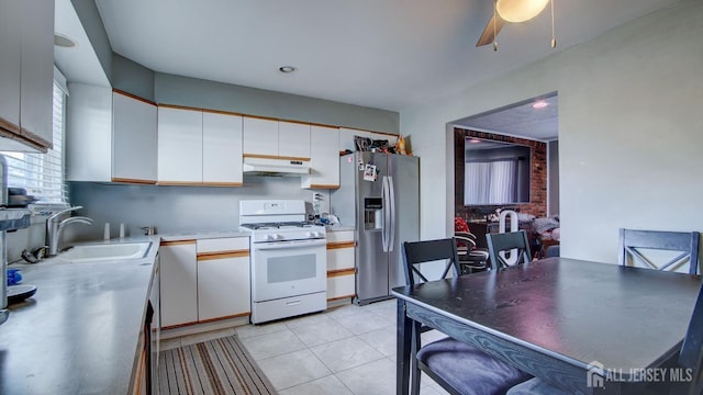 kitchen featuring gas range gas stove, light tile patterned flooring, a sink, white cabinets, and stainless steel fridge