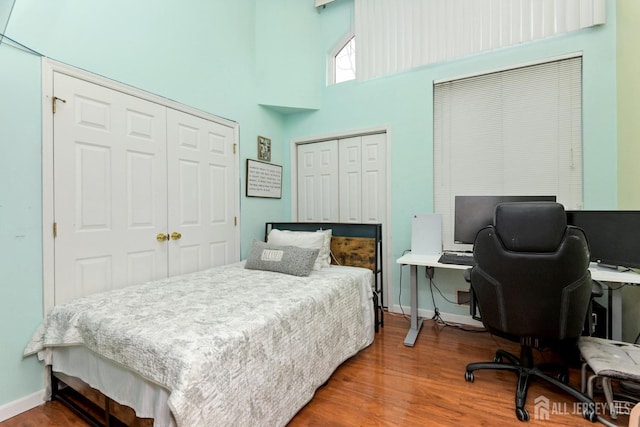 bedroom featuring a towering ceiling, wood finished floors, baseboards, and a desk