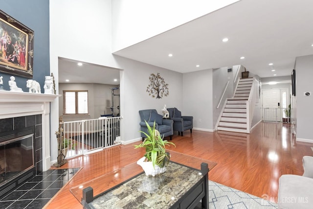 living area with stairs, recessed lighting, wood finished floors, a tiled fireplace, and baseboards