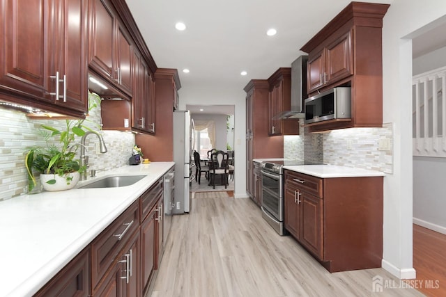 kitchen featuring a sink, stainless steel appliances, wall chimney exhaust hood, light wood-type flooring, and baseboards