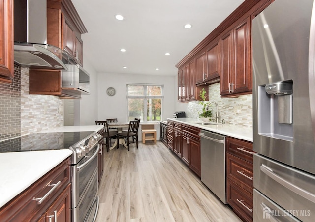 kitchen featuring stainless steel appliances, wall chimney exhaust hood, a sink, decorative backsplash, and recessed lighting
