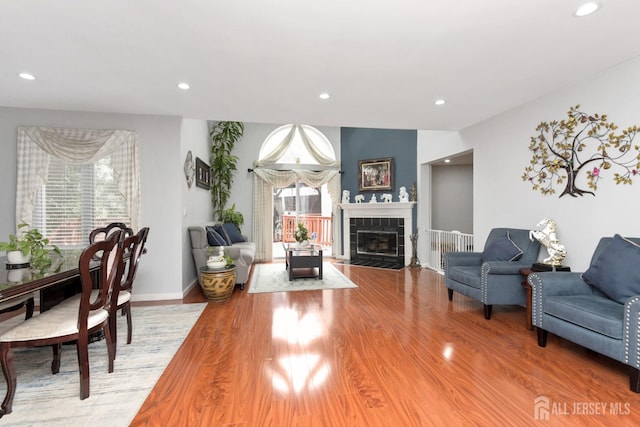 living room featuring healthy amount of natural light, light wood-style floors, recessed lighting, a tiled fireplace, and baseboards