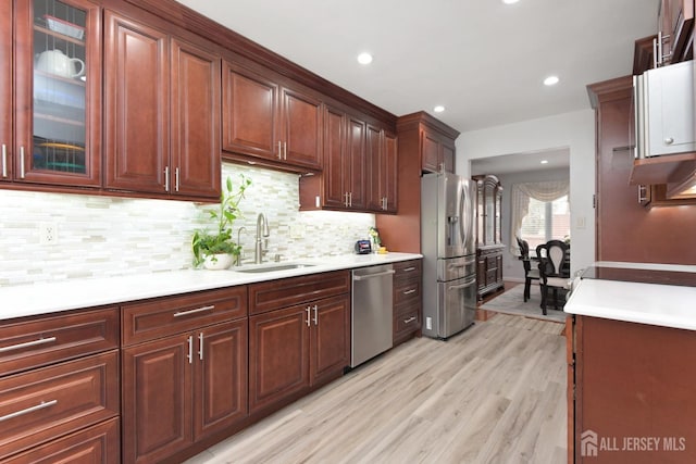kitchen with appliances with stainless steel finishes, a sink, light wood-style floors, light countertops, and backsplash