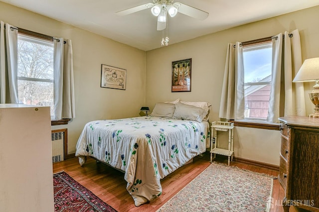 bedroom with multiple windows, radiator, wood finished floors, and baseboards