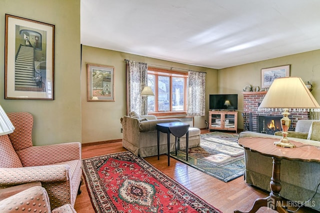 living room featuring a brick fireplace, baseboards, and wood finished floors