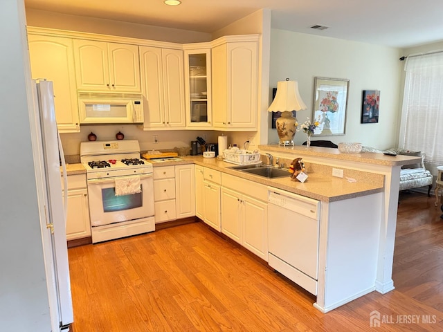 kitchen featuring a sink, white appliances, light wood-style flooring, a peninsula, and visible vents