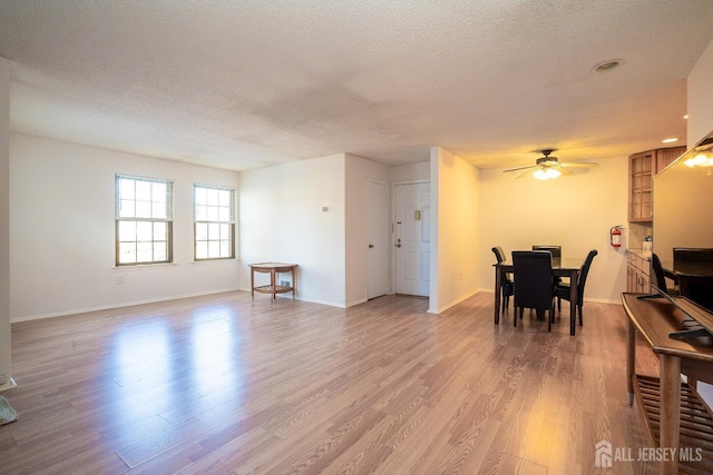 dining room with a textured ceiling, light wood-type flooring, a ceiling fan, and baseboards