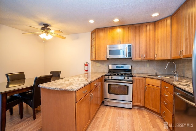 kitchen with stainless steel appliances, brown cabinetry, a sink, and a peninsula