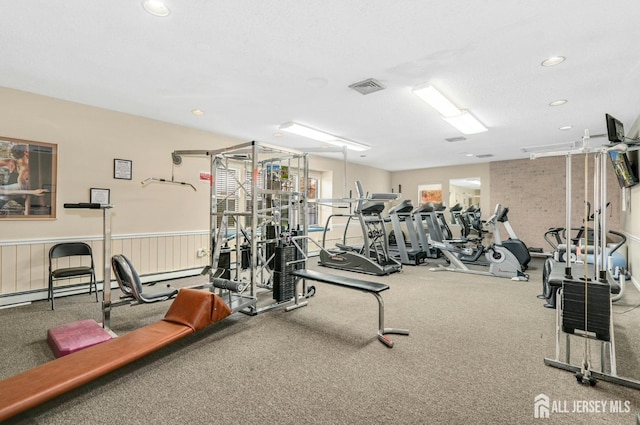 gym with a textured ceiling, wainscoting, visible vents, and recessed lighting