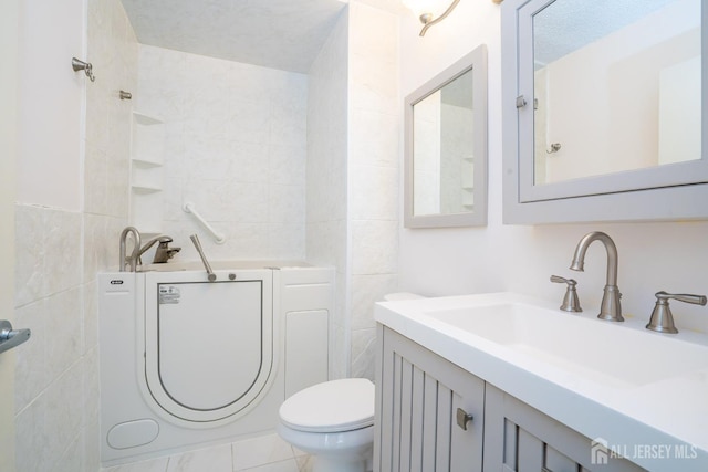 bathroom featuring washer / dryer, toilet, a textured ceiling, vanity, and tile walls