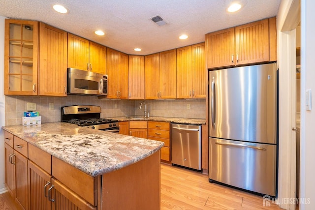 kitchen with visible vents, glass insert cabinets, appliances with stainless steel finishes, light stone counters, and light wood-style floors