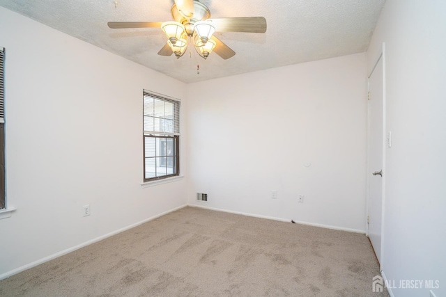 spare room featuring light carpet, a textured ceiling, visible vents, and baseboards