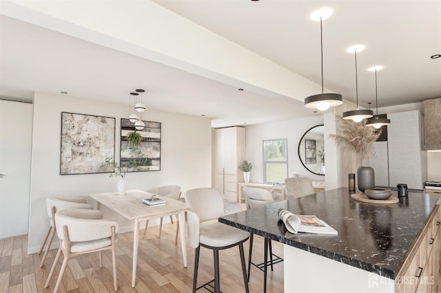 kitchen featuring pendant lighting, a breakfast bar, light wood-style flooring, a center island, and dark stone counters