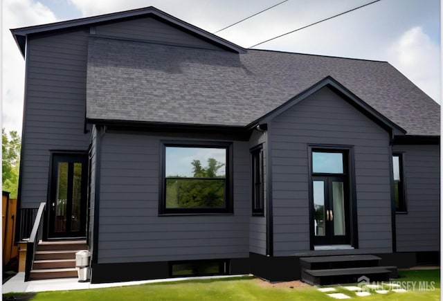 rear view of house with a lawn, entry steps, and roof with shingles