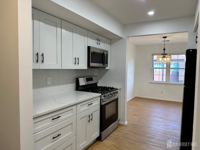 kitchen with light stone counters, white cabinets, light wood-style floors, appliances with stainless steel finishes, and backsplash