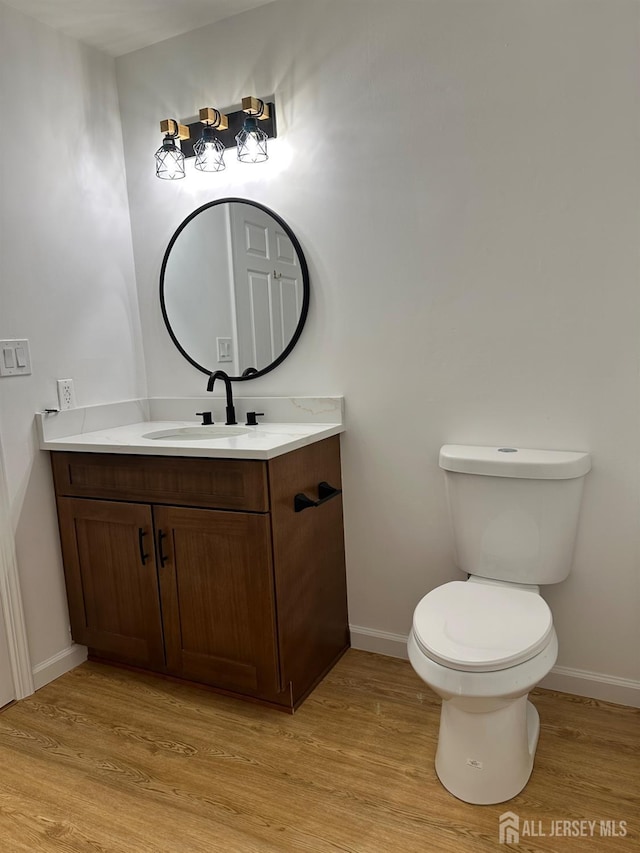 half bath featuring vanity, toilet, wood finished floors, and baseboards