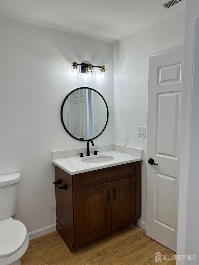 half bathroom featuring vanity, toilet, wood finished floors, and baseboards