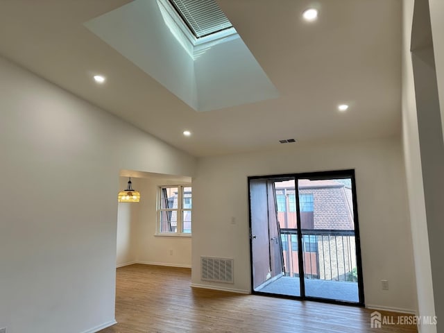 unfurnished room with visible vents, baseboards, vaulted ceiling with skylight, recessed lighting, and wood finished floors