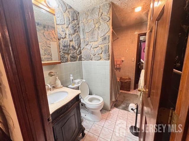 bathroom with toilet, tile patterned flooring, a textured ceiling, vanity, and tile walls