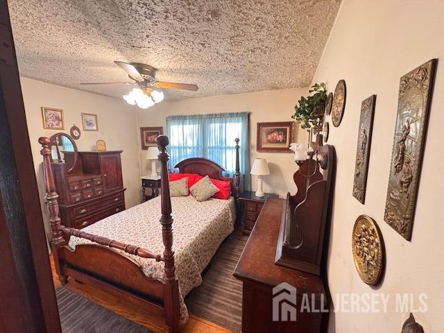 bedroom featuring a textured ceiling, ceiling fan, and dark wood finished floors