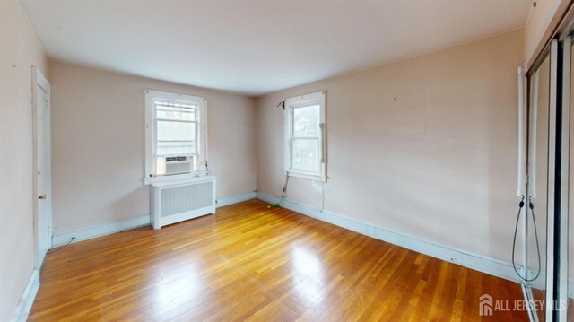 unfurnished bedroom featuring cooling unit, radiator heating unit, light hardwood / wood-style floors, and a closet