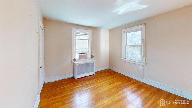 empty room featuring cooling unit, plenty of natural light, radiator heating unit, and light hardwood / wood-style flooring