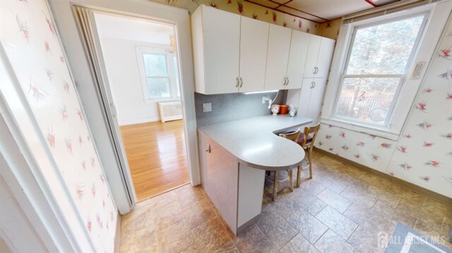 kitchen with radiator, kitchen peninsula, white cabinets, and a kitchen bar