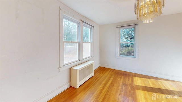 empty room with radiator, a notable chandelier, and light hardwood / wood-style flooring