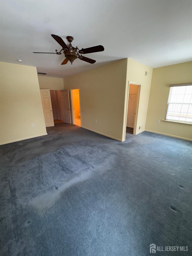 empty room featuring a ceiling fan, dark colored carpet, visible vents, and baseboards