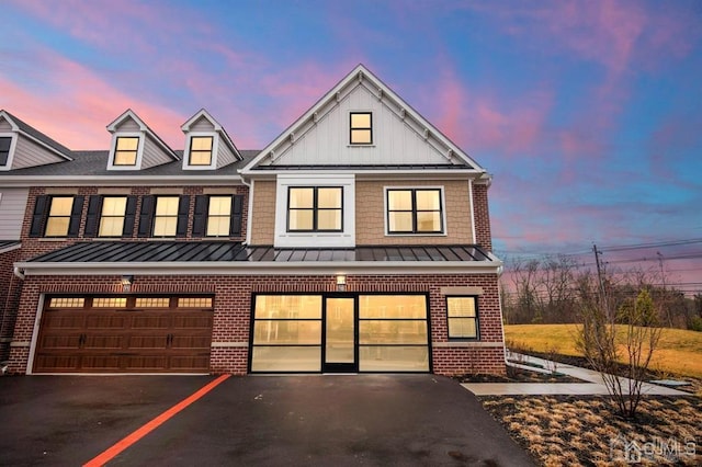 multi unit property with driveway, a standing seam roof, board and batten siding, an attached garage, and brick siding