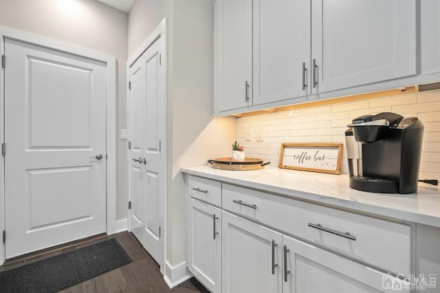bar featuring dark wood-type flooring, backsplash, and baseboards
