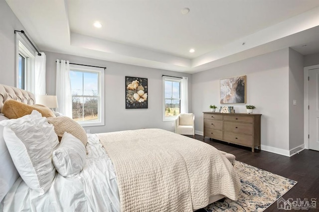 bedroom featuring a raised ceiling, multiple windows, baseboards, and dark wood-style flooring