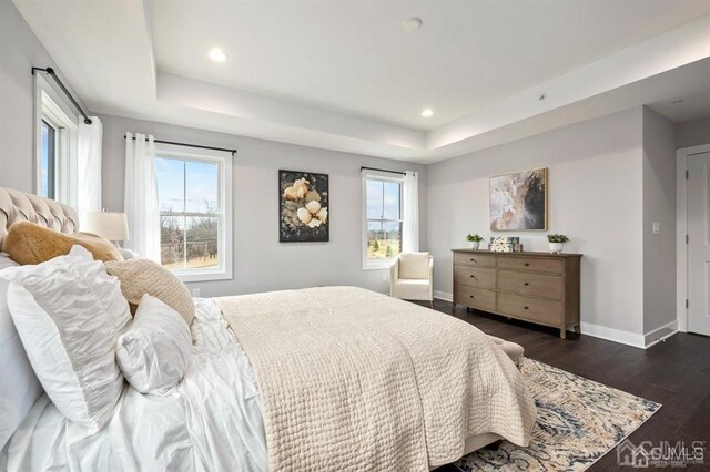 bedroom with a raised ceiling, dark wood-style flooring, baseboards, and recessed lighting