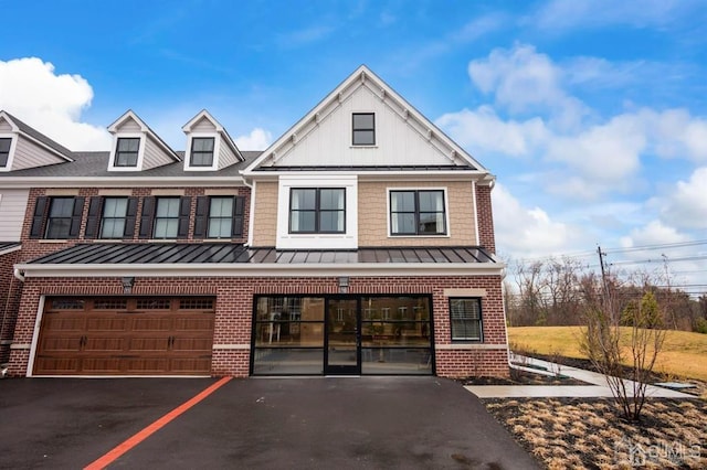 townhome / multi-family property featuring brick siding, driveway, a standing seam roof, and board and batten siding