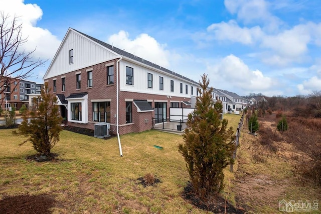 rear view of property featuring board and batten siding, a yard, fence, and brick siding