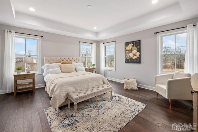 bedroom with dark wood-type flooring, multiple windows, baseboards, and a raised ceiling