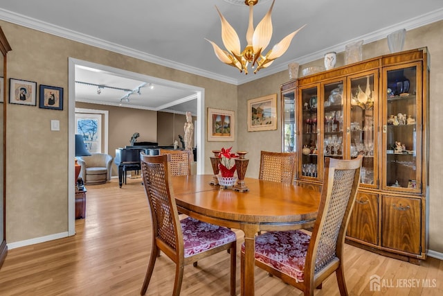 dining area with an inviting chandelier, crown molding, track lighting, and light hardwood / wood-style floors