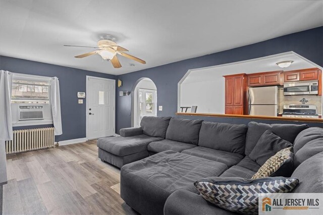 living room featuring ceiling fan, radiator heating unit, light hardwood / wood-style floors, and cooling unit