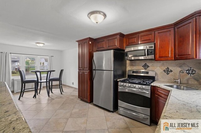 kitchen featuring stainless steel appliances, light stone countertops, sink, and backsplash