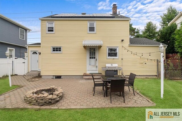 back of property featuring solar panels, a fire pit, a yard, and a patio area