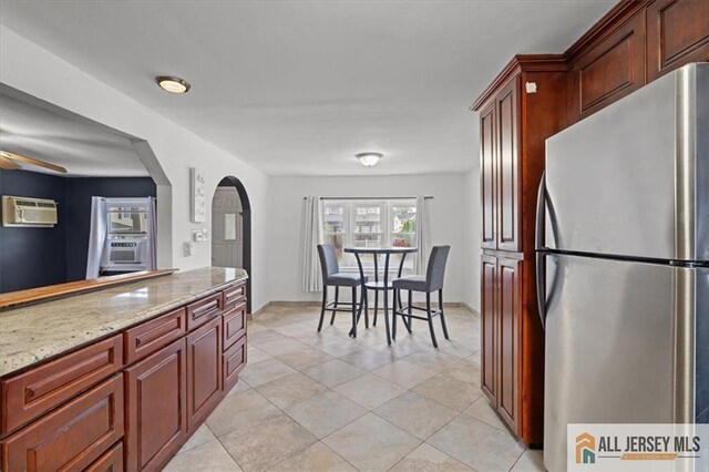 kitchen with light tile patterned flooring, a wall mounted AC, stainless steel fridge, ceiling fan, and light stone countertops