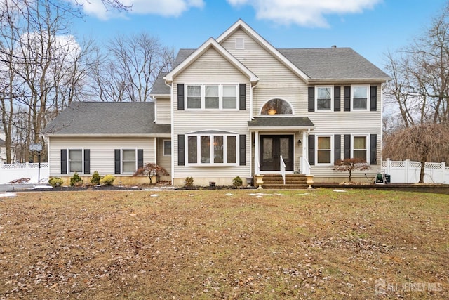 view of front facade with a shingled roof, fence, and a front lawn