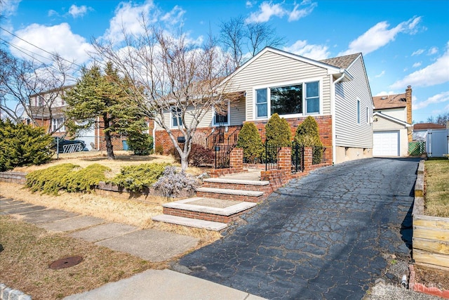 view of front facade featuring brick siding, a detached garage, fence, aphalt driveway, and an outdoor structure