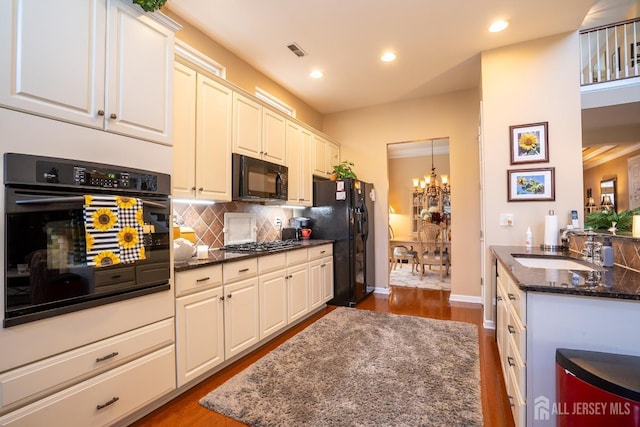 kitchen featuring sink, white cabinetry, dark stone counters, a notable chandelier, and black appliances